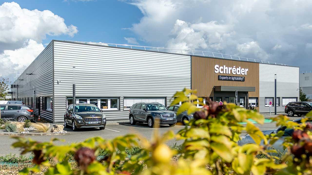 usine Comatelec Schréder Bourges voiture garées sur un parking feuillage au premier plan 