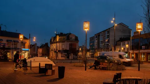 place éclairée par des luminaires BOREAL et YOA, personnes assises sur un banc 