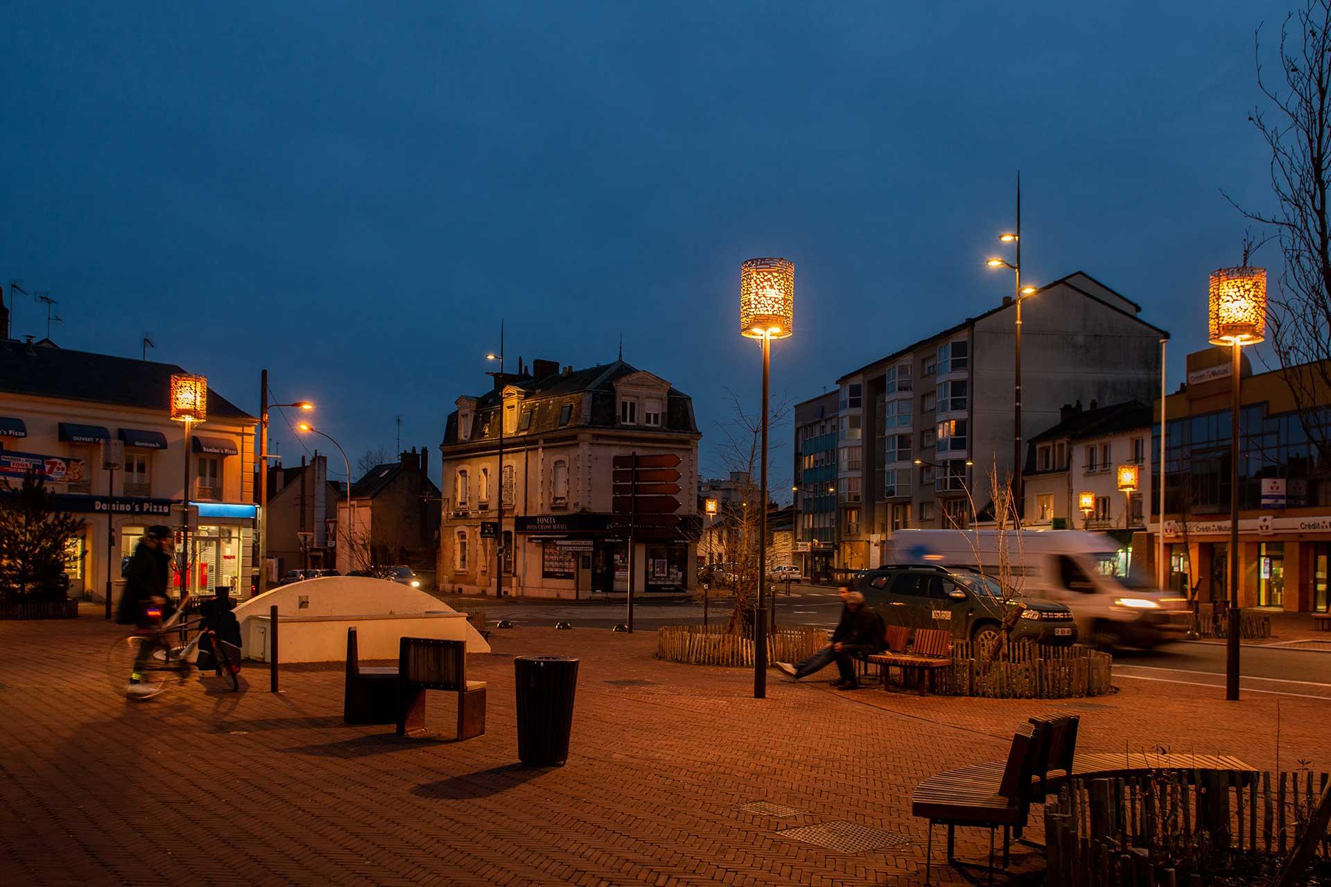 place éclairée par des luminaires BOREAL et YOA, personnes assises sur un banc 